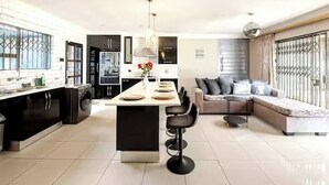 Una cocina moderna con una isla central, un comedor con sofá y una sala de estar con televisor.