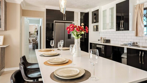Una cocina moderna con una isla central, armarios negros y encimera blanca.