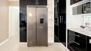 Una cocina moderna con un refrigerador de acero inoxidable, gabinetes negros y una encimera blanca.