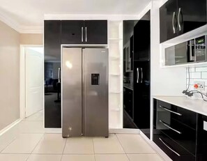 A modern kitchen with a stainless steel refrigerator, black cabinetry, and a white countertop.