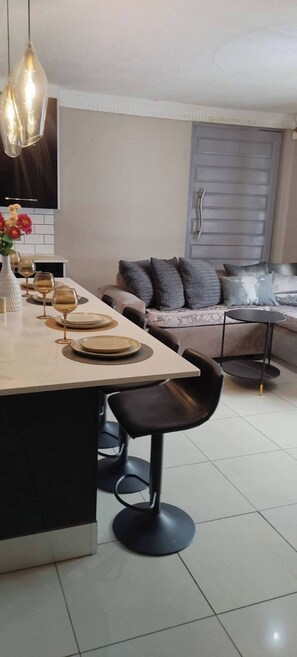 Una cocina moderna con una isla central, taburetes negros y un comedor con sofá y mesa.