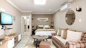 Habitación de hotel con cama, sofá, mesa de centro, televisor y aire acondicionado.