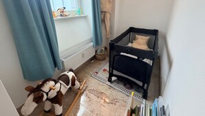 Una culla per bambini, un cavalluccio a dondolo e una finestra con tende in una stanza.