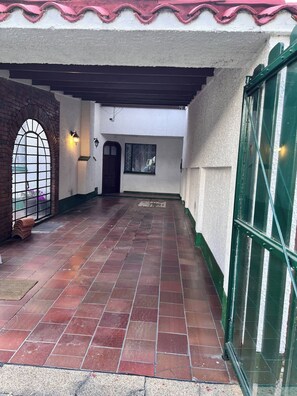 Ein überdachter Außenbereich mit Fliesenboden, einem Ziegelbogen, einer Tür und einem Fenster mit Gitter.