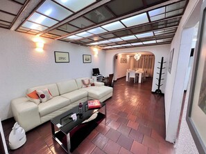 Ein Wohnzimmer mit einer Eckcouch, einem Glastisch und einem Essbereich mit einer Pendelleuchte.