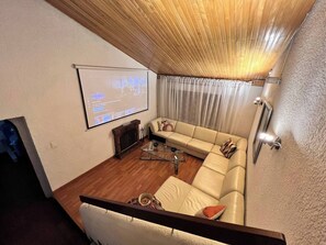 Ein Wohnzimmer mit Ecksofa, Kamin, Wandfernseher und einer Treppe, die eine weitere Ebene hinaufführt.