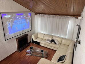 Un saló amb televisió de pantalla plana, un sofà beix, una taula de centre de vidre i una llar de foc.