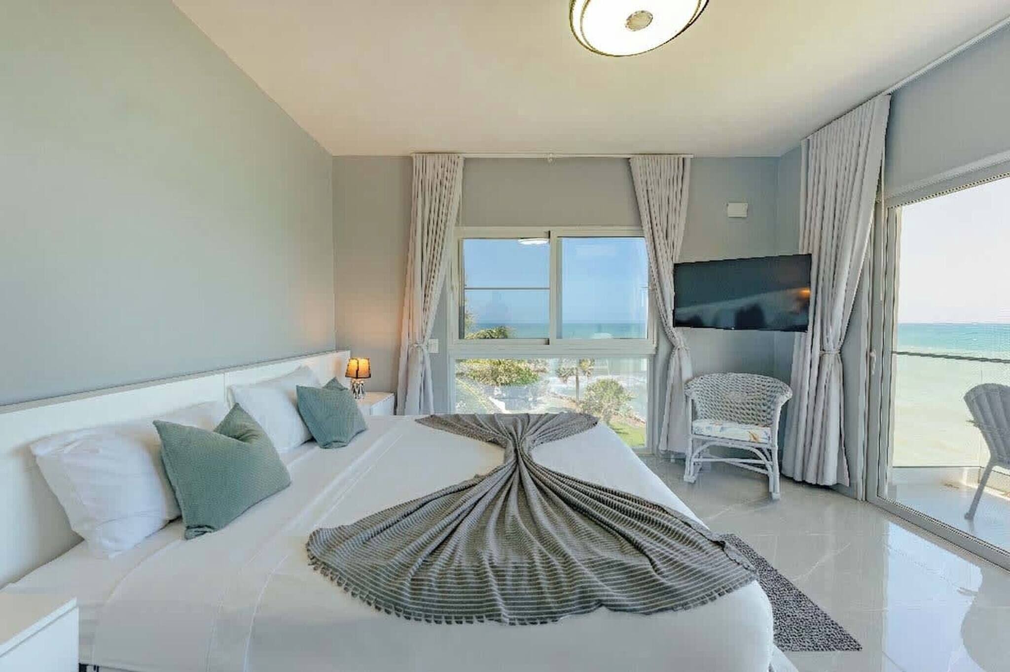 A hotel room with a bed, a television, a chair, and a view of the sea.