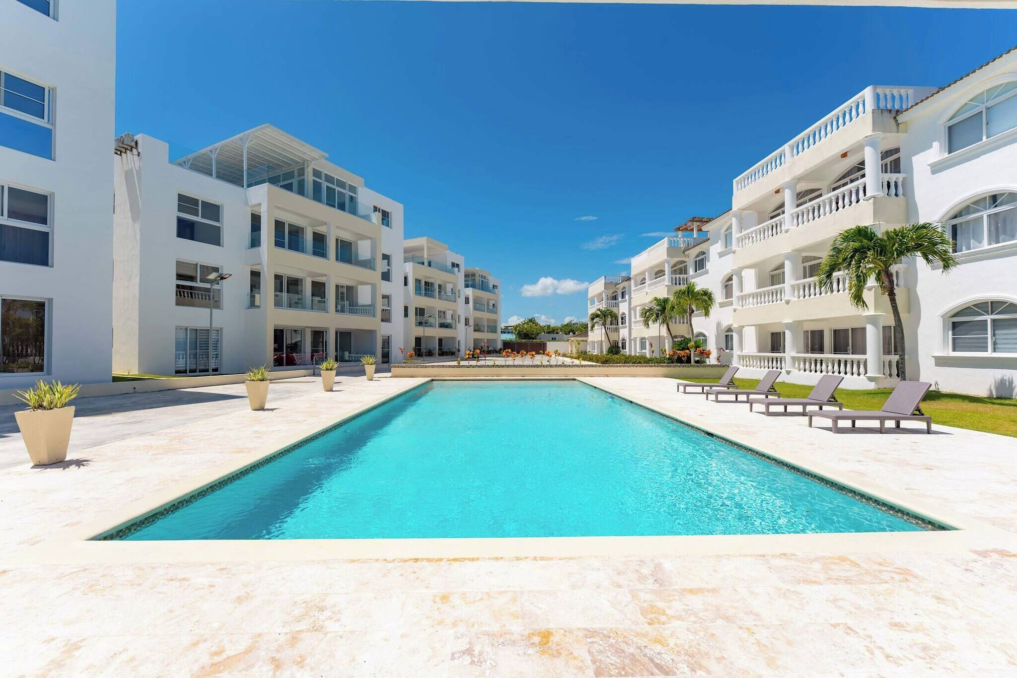 Una piscina con sillas de descanso, edificios blancos y palmeras.