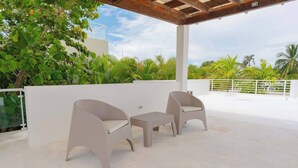 Eine Terrassenanlage im Freien mit zwei Korbstühlen und einem kleinen Tisch, umgeben von üppiger Bepflanzung und einer weißen Mauer.