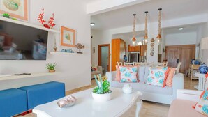 Ein modernes Wohnzimmer mit einem weißen Sofa, blauen Sitzgelegenheiten, einem weißen Couchtisch und einem Küchenbereich im Hintergrund.
