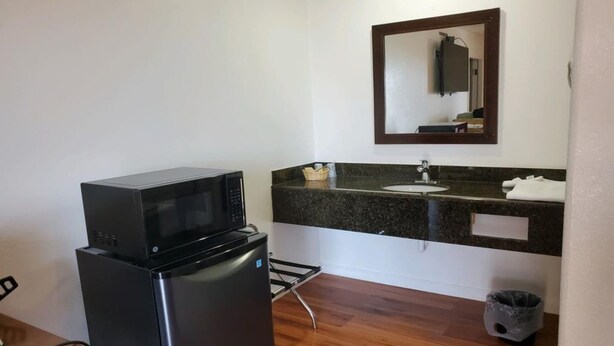 A compact kitchenette with a microwave, refrigerator, sink, and a trash bin.