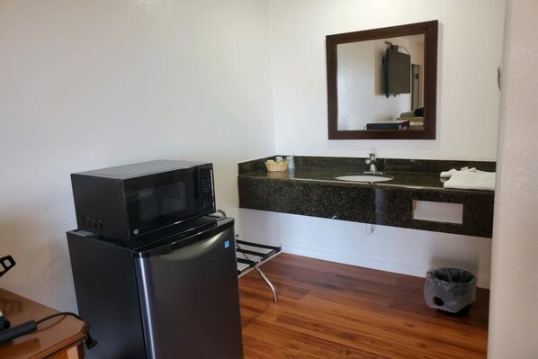 A compact kitchenette with a microwave, refrigerator, sink, and a trash bin.