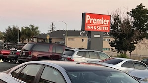 En parkeringsplads med flere biler, et skilt for Premier Inn & Suites, og en bygning i baggrunden.