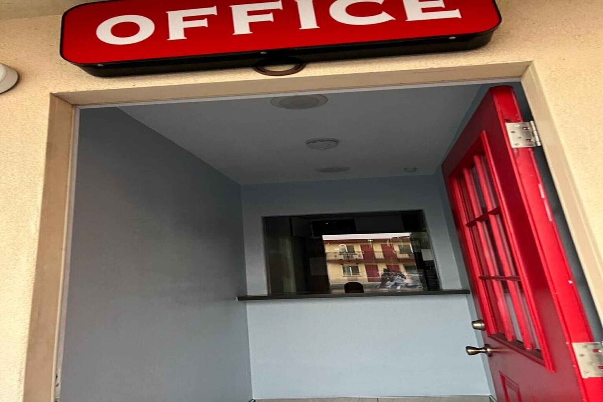 An office entrance with a red door and a window overlooking a building.