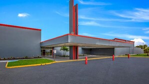 Un edifici modern amb zona de pàrquing coberta, una estructura vertical alta i un cel clar.