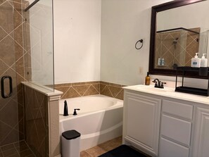 A bathroom with a bathtub, a glass shower enclosure, a sink with a mirror, and a trash bin.