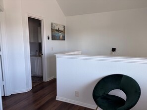 A room with a white wall, a door leading to a kitchen, and a dark green circular object on the floor.