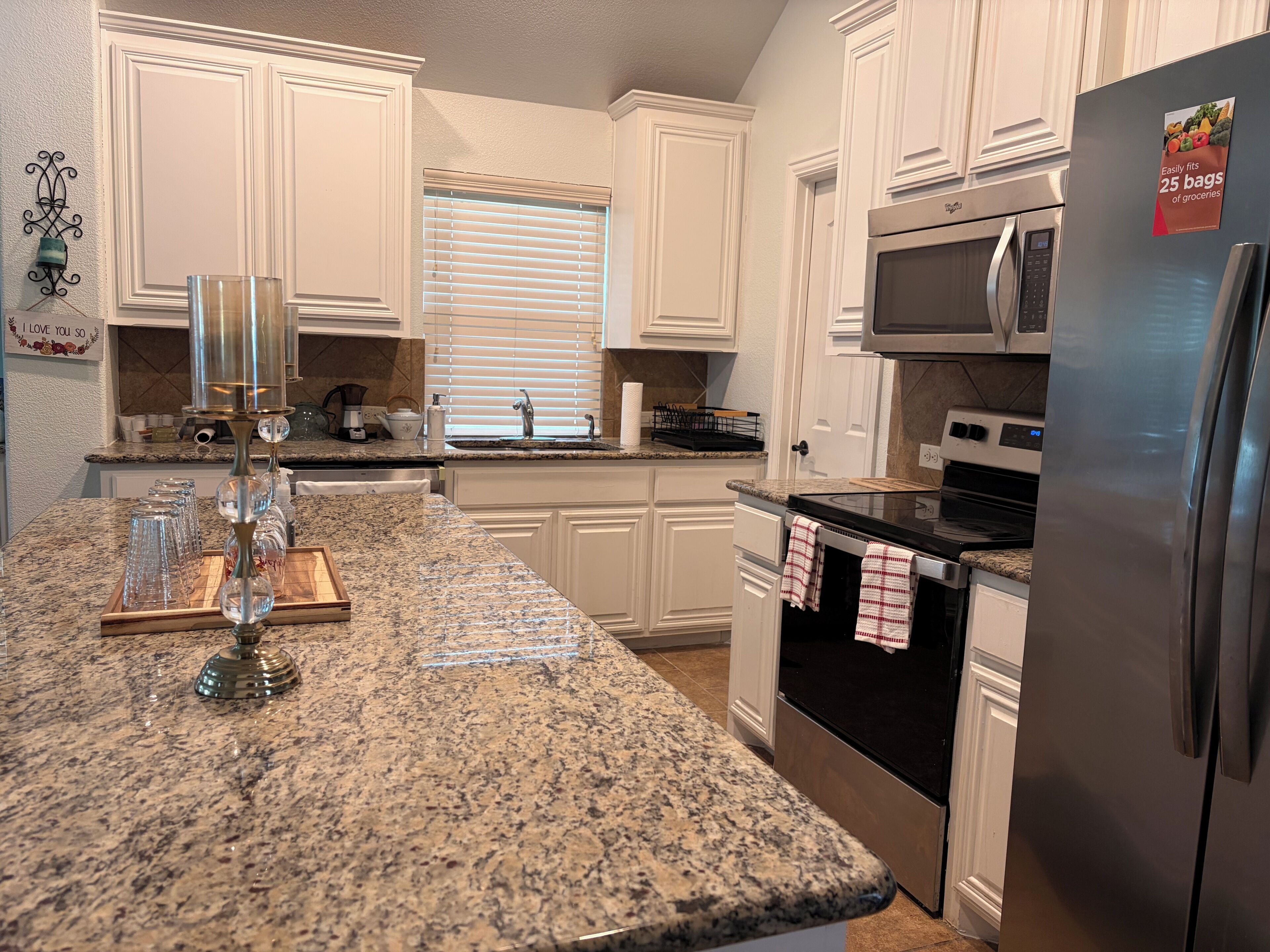 A kitchen with white cabinets, granite countertops, stainless steel appliances, and a window with blinds.