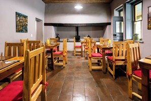 A dining area with wooden tables and chairs, a fireplace, and a view of the outside through a window.