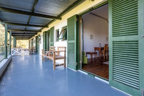 A covered outdoor seating area with wooden benches and tables, green shutters, and a white brick wall interior.