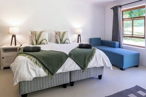 Un dormitorio con cama, mesitas de noche, lámparas, un sofá azul y una ventana con cortinas.