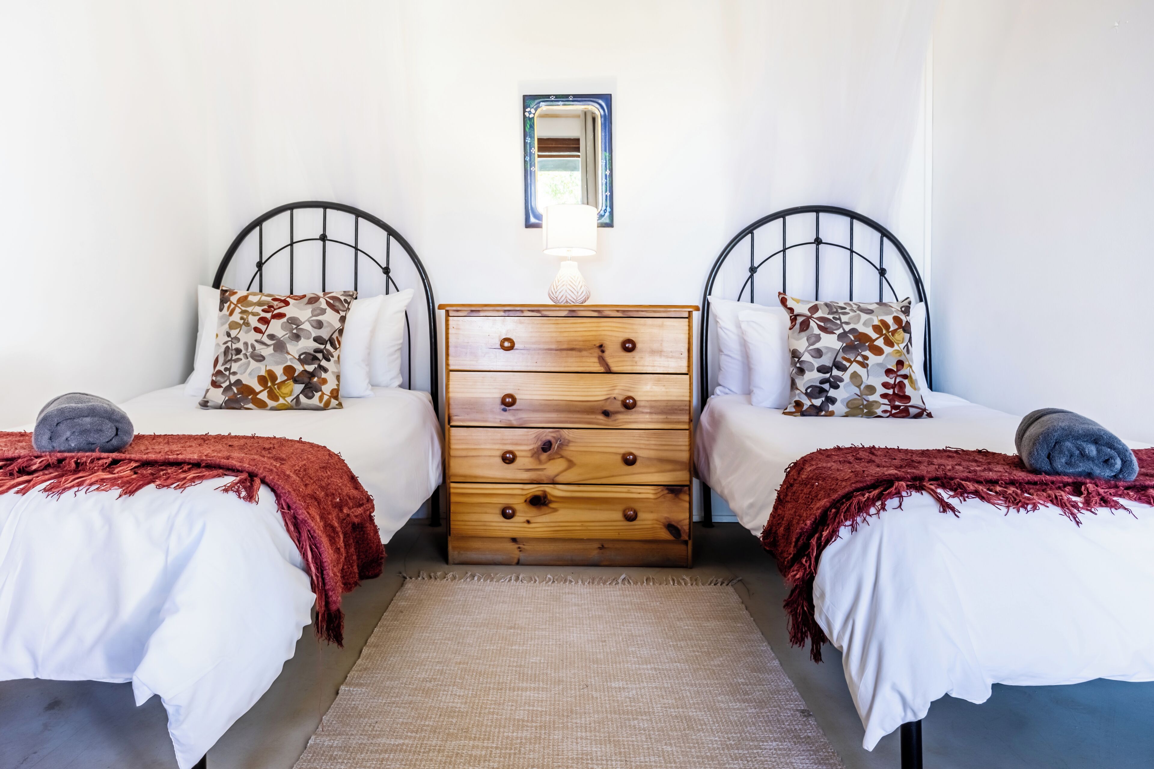 Une chambre avec deux lits, une commode en bois et un miroir au mur.