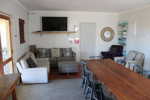 A living room with a sofa, ottoman, and a wooden dining table with chairs. - Goedgedacht Farm (WC)