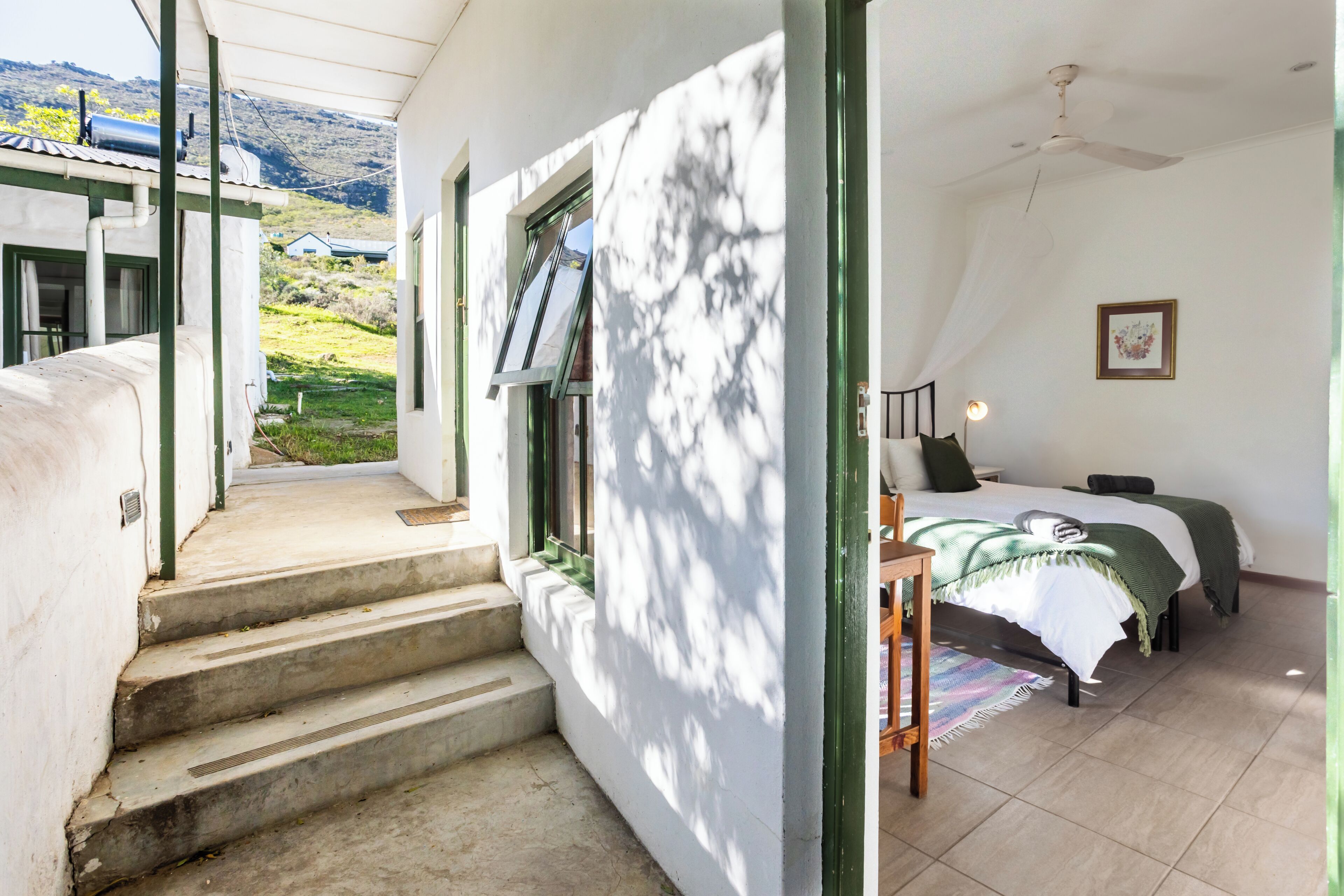 Quarto com uma cama, mesa de cabeceira e janela com vista para uma encosta.