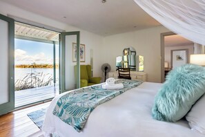 A bedroom with a bed, a green chair, a fan, and a view of a body of water.