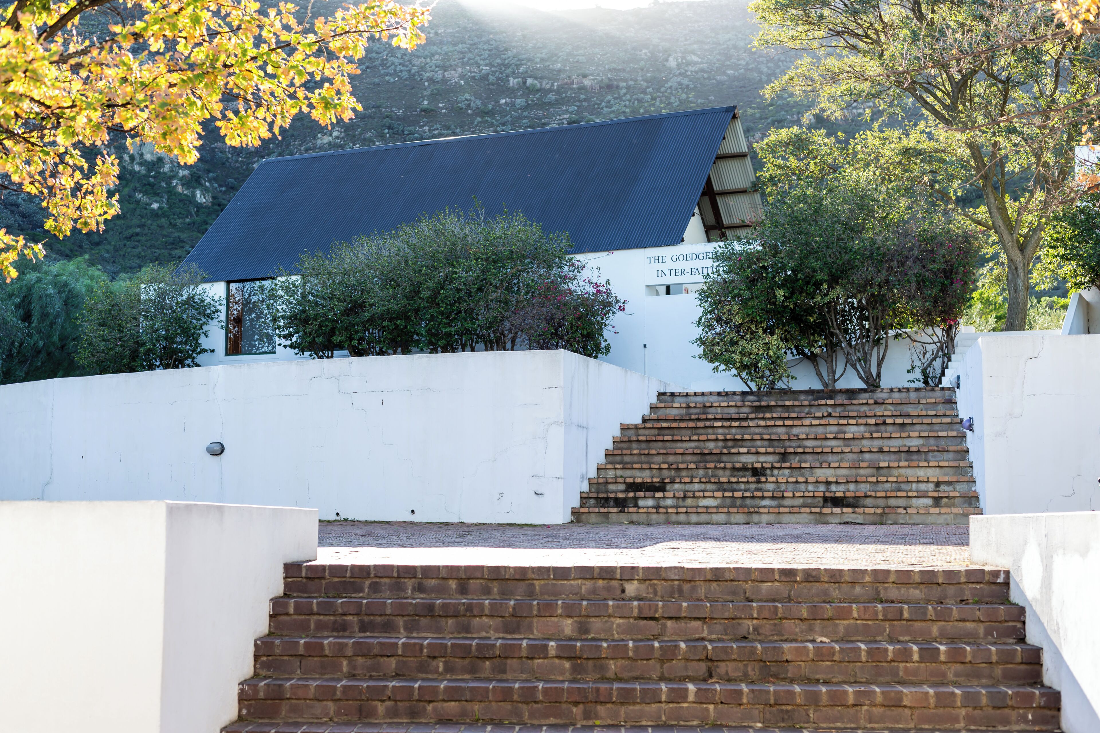 A building with a blue roof and a white wall, surrounded by trees and a brick staircase leading up to it.