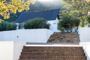 A building with a blue roof and a white wall, surrounded by trees and a brick staircase leading up to it. - Goedgedacht Farm (WC)
