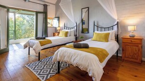 A bedroom with two beds, a wooden floor, a patterned rug, and a view of greenery outside.