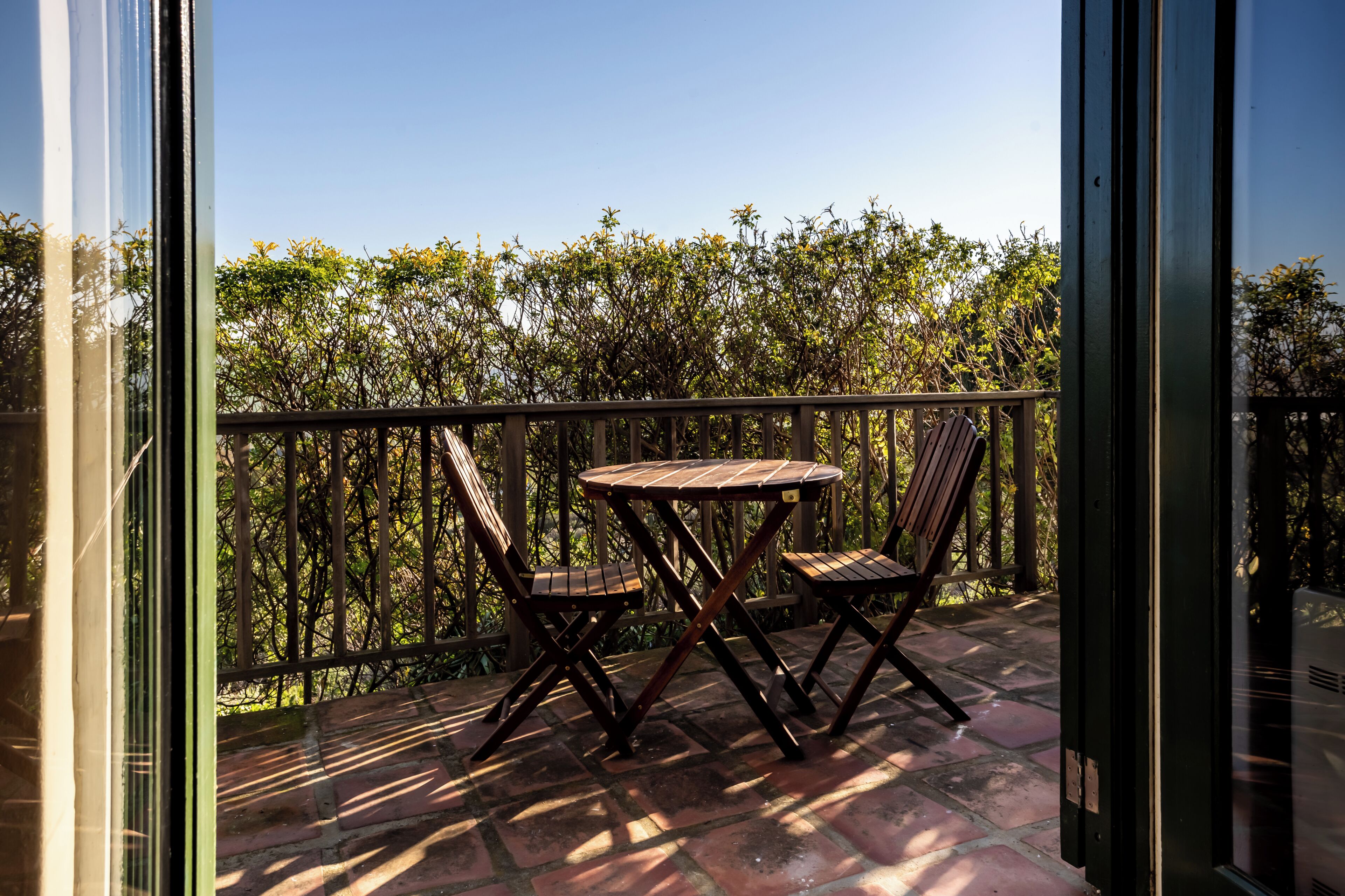 Un balcon avec une table et deux chaises, donnant sur une haie touffue.