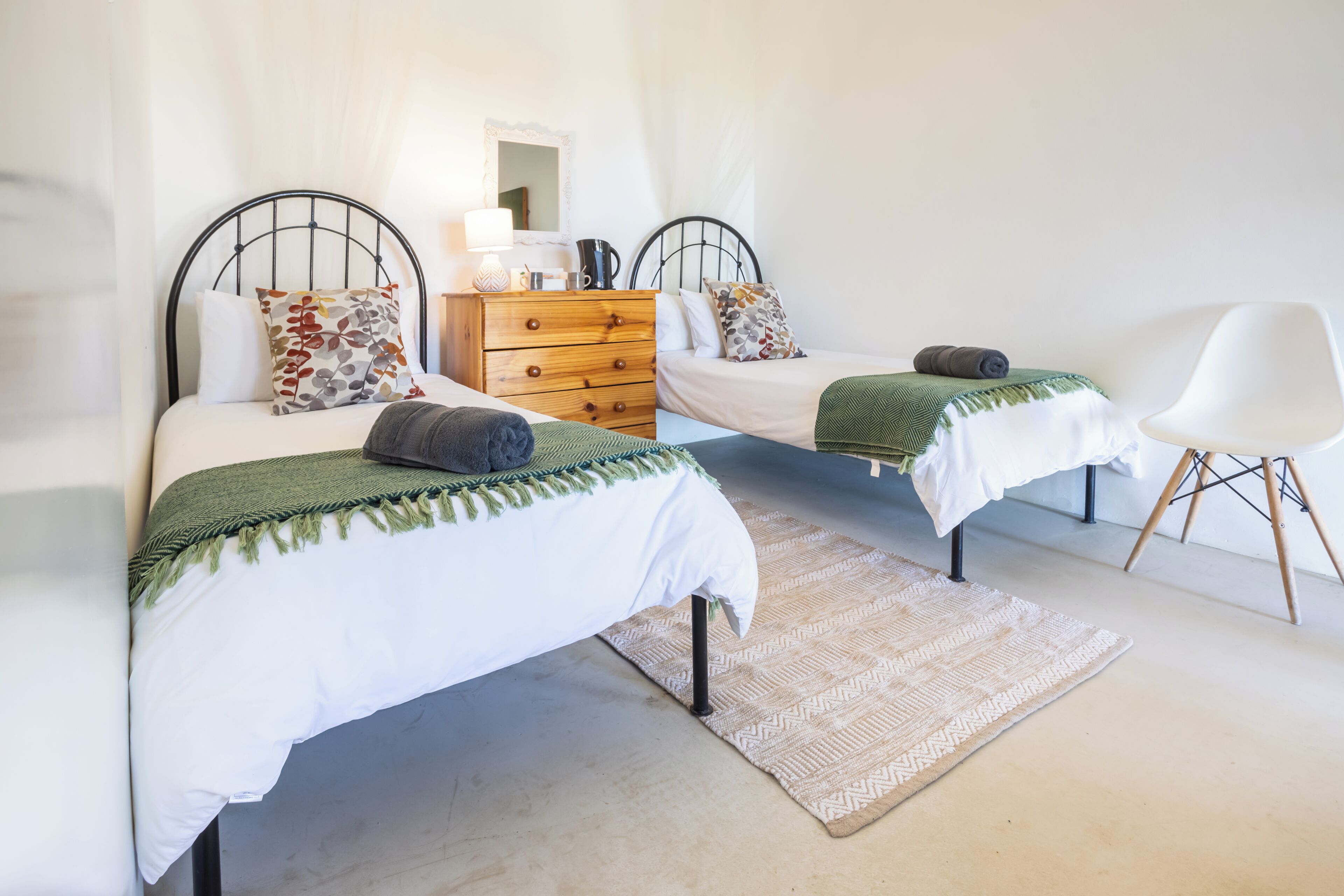 Un dormitorio con dos camas individuales, un aparador de madera, una silla blanca y una alfombra estampada.