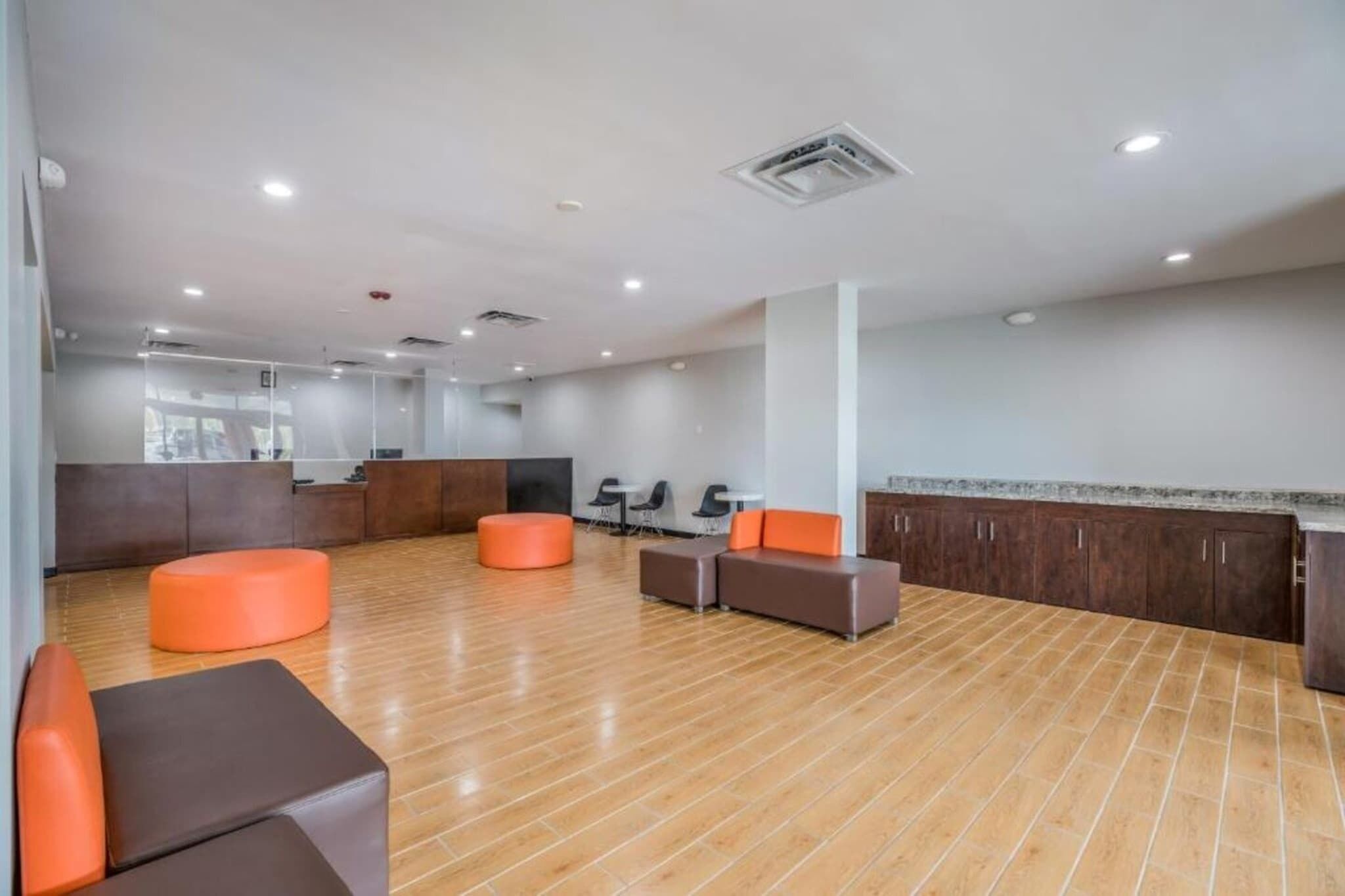 A spacious lobby with wooden flooring, orange and brown seating, a reception desk, and a large window.