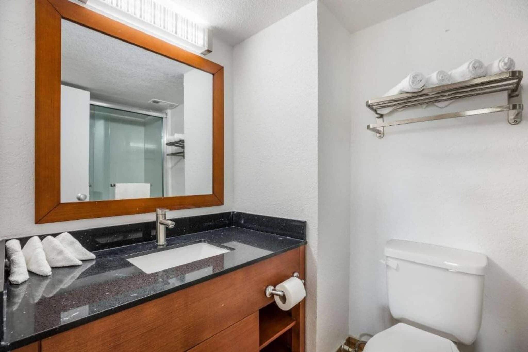 A bathroom with a sink, mirror, toilet, and towel rack.