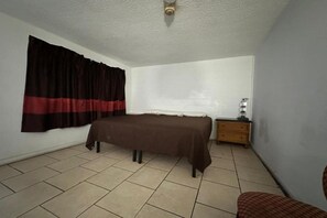 Ein Schlafzimmer mit einem Bett, einem Nachttisch, einem Sessel und einem Fenster mit Vorhängen.