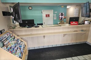A reception desk with a clock, a 'Check Out' sign, a 'No Refunds' sign, and a computer monitor.