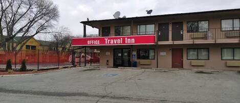 Een Travel Inn met een rood bord, meerdere ramen en een omheind parkeerterrein.