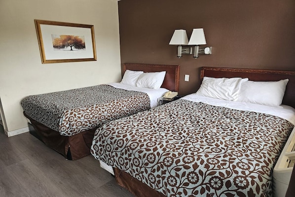 Two double beds with patterned bedding, a framed picture on the wall, and two wall-mounted lamps.