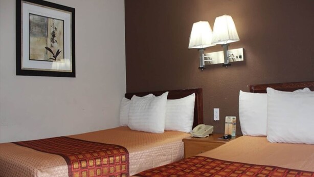 Habitación de hotel con dos camas, una obra de arte enmarcada en la pared y una lámpara fijada a la pared.
