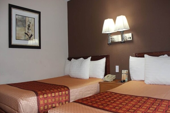 A hotel room with two beds, a framed artwork on the wall, and a wall-mounted lamp.