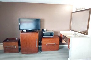 A compact room with a wooden cabinet, a television, a microwave, a small drawer, and a mirror.