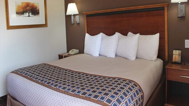 Una habitación de hotel con una cama grande, dos lámparas de noche, una mesita de noche, un cuadro en la pared y un teléfono sobre la mesita.