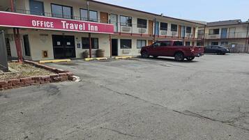 A motel with a red awning labeled 'OFFICE Travel Inn,' a parking lot, and a red pickup truck parked in front.