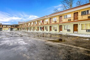 Eine Reihe von Motelzimmern mit individuellen Eingängen und Fenstern, ein Parkplatz mit Pfützen und ein klarer Himmel.