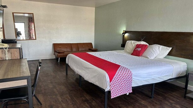 Une chambre d’hôtel avec un lit, un bureau en bois, une chaise, un canapé et un miroir.