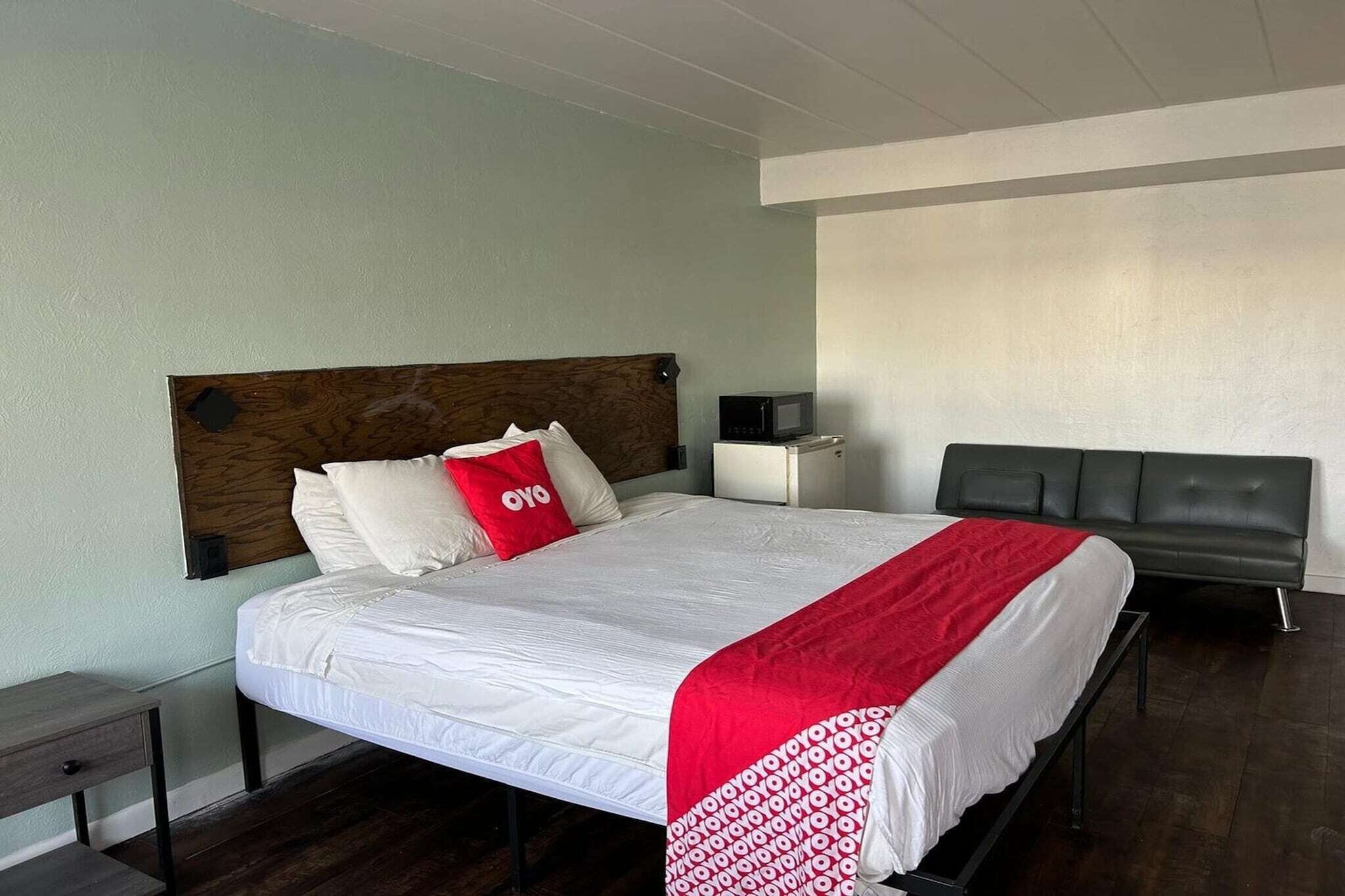 A hotel room with a bed, bedside table, lamp, and a black leather sofa.