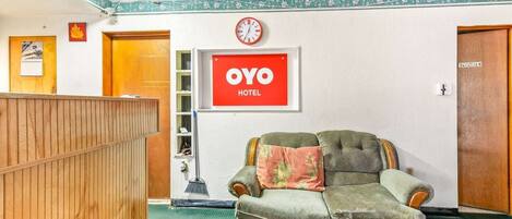 A reception area with a wooden desk, a green sofa, a clock, and a sign that reads 'OYO HOTEL.'